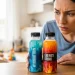 A concerned parent looking at two similar bottles labeled hydration and energy drink, colorful drink bottles on table, child in background, bright lighting, realistic photo, blog thumbnail style