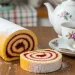 “Golden spiral jelly roll cake dusted with sugar, sliced to show jam swirl, soft natural light, rustic kitchen table, tea setting, high detail food photography”